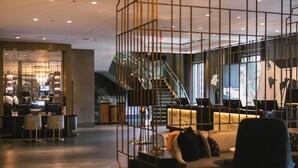 A modern hotel lobby with a reception desk, seating area, staircase, and large windows.