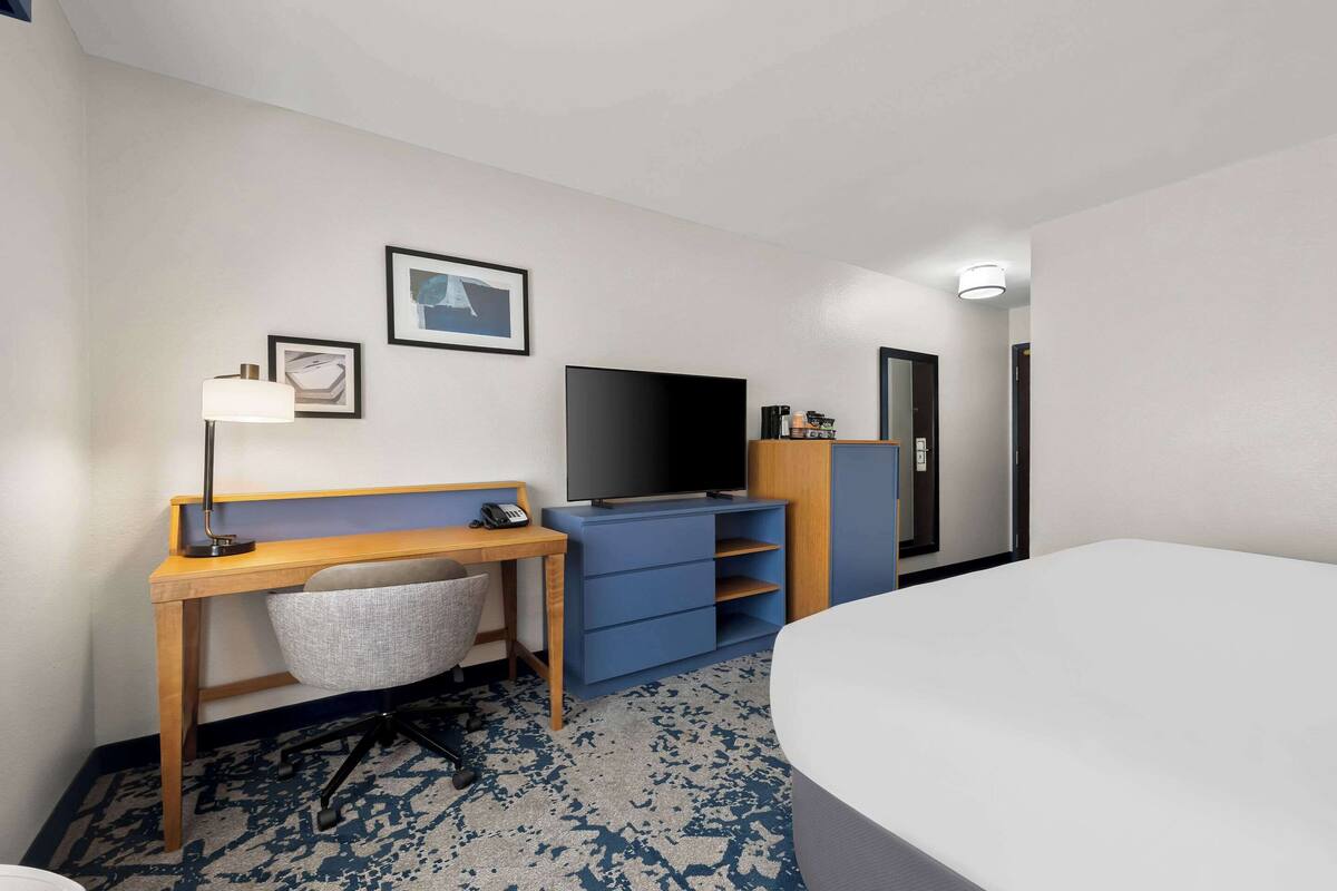Una habitación de hotel con cama, escritorio con silla, televisor, armario y una lámpara de escritorio.