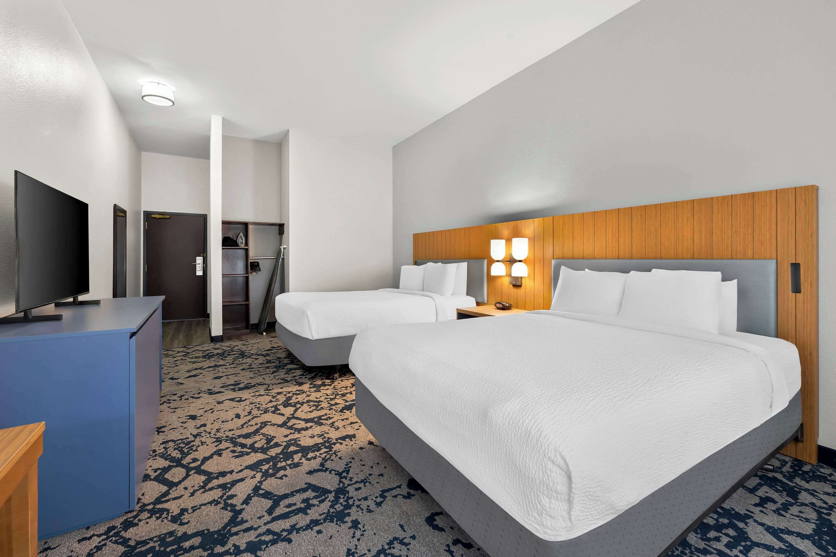 A hotel room with two beds, a desk, a television, and a bathroom visible through an open door.