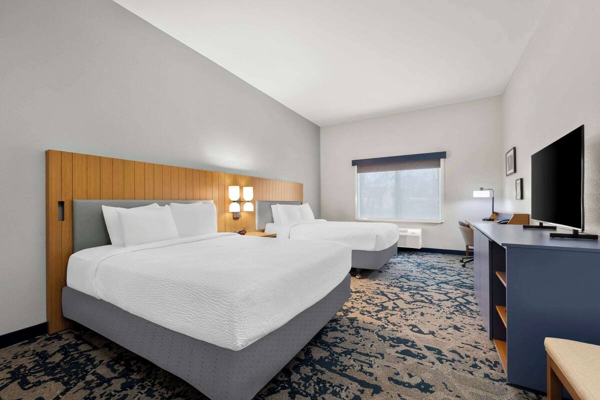 Habitación de hotel con dos camas, un escritorio, un televisor y una ventana.