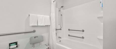 Un baño con bañera, barras de apoyo, una silla accesible para silla de ruedas y un perchero para toallas.