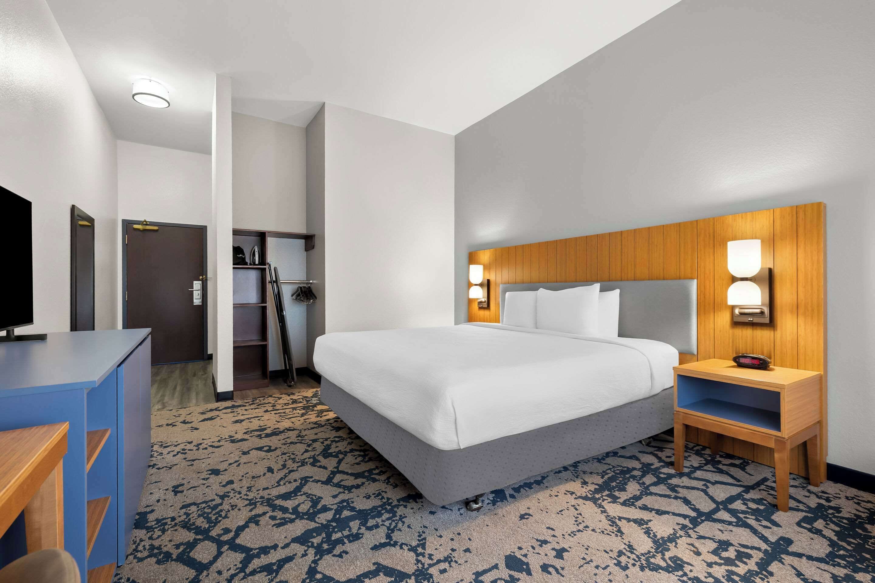 A hotel room with a large bed, a wooden headboard, bedside lamps, a desk, and a television.