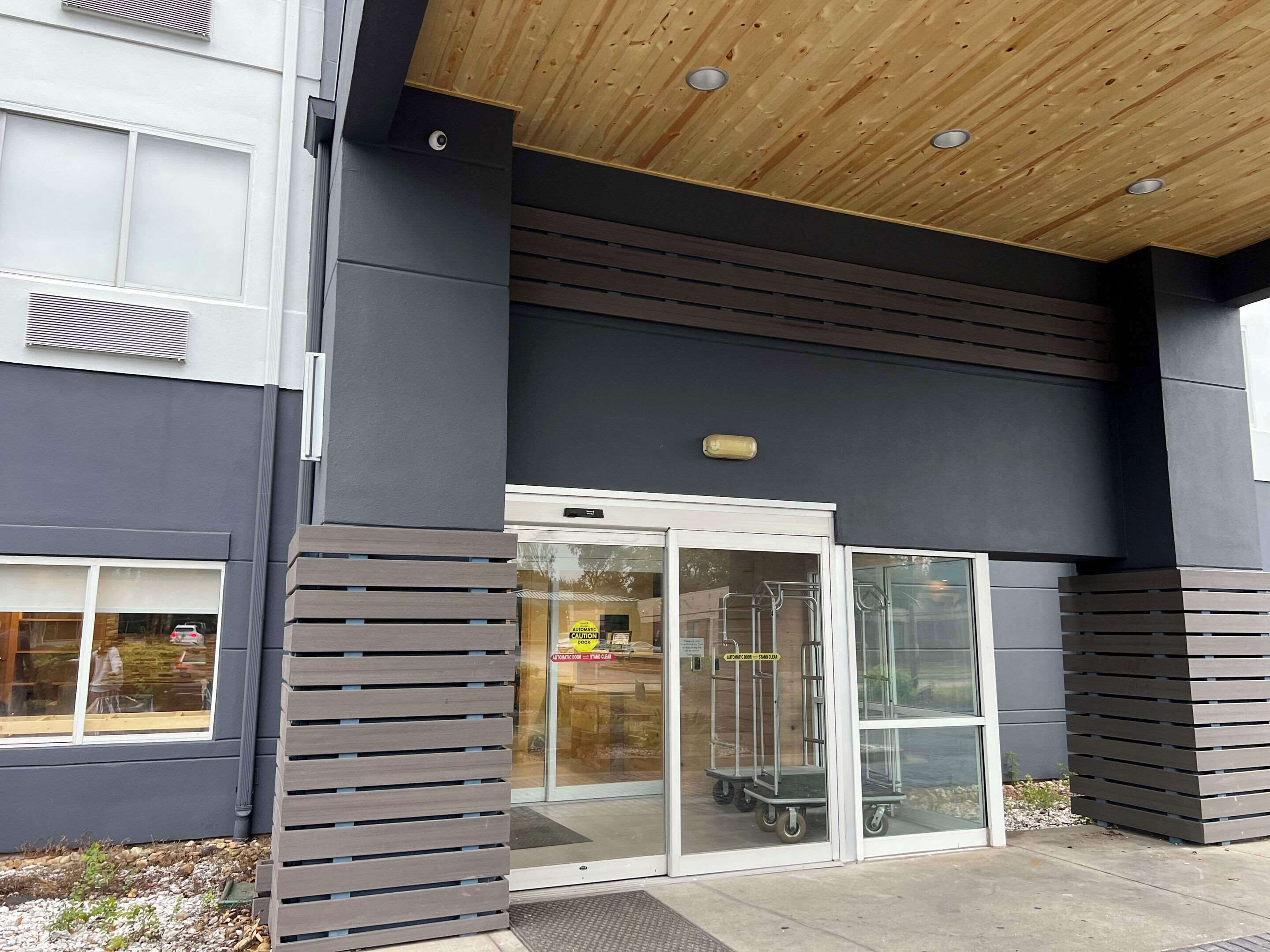A building entrance with a glass door, a wooden ceiling, and a metal sign above the door.