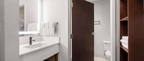 A modern bathroom with a white sink, a mirror, and a wooden door leading to a shower area.