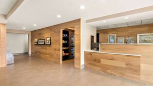 Uma área de recepção com painéis de madeira, balcão de atendimento e um refrigerador repleto de lanches.