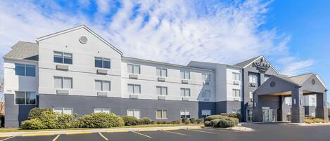 A modern hotel with a two-story structure, a parking lot, and a covered entrance.
