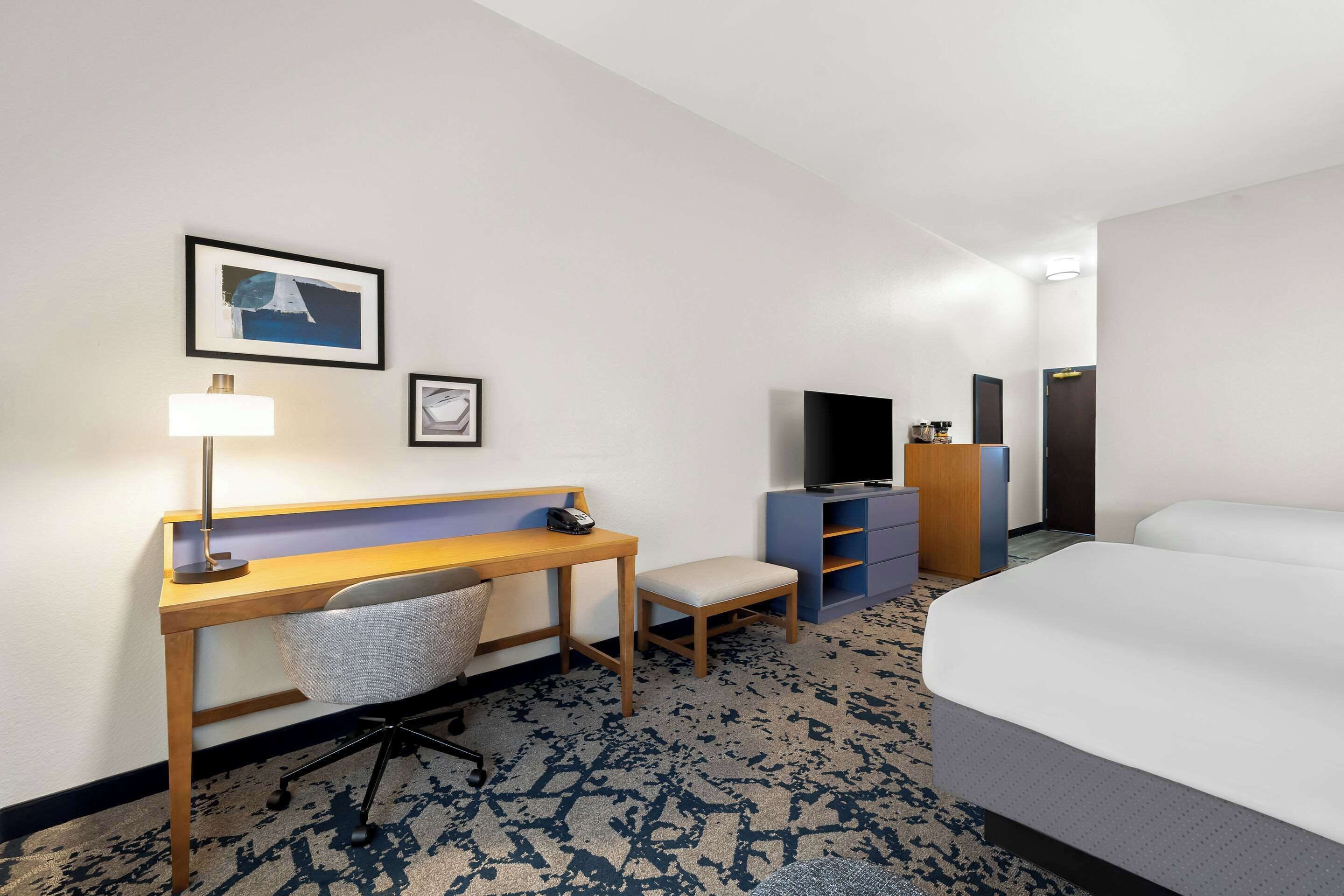 A hotel room with a bed, a desk with a chair, a TV, and a small seating area.