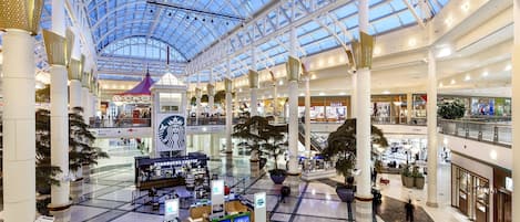 A multi-level shopping mall with a glass ceiling, various stores, and seating areas.