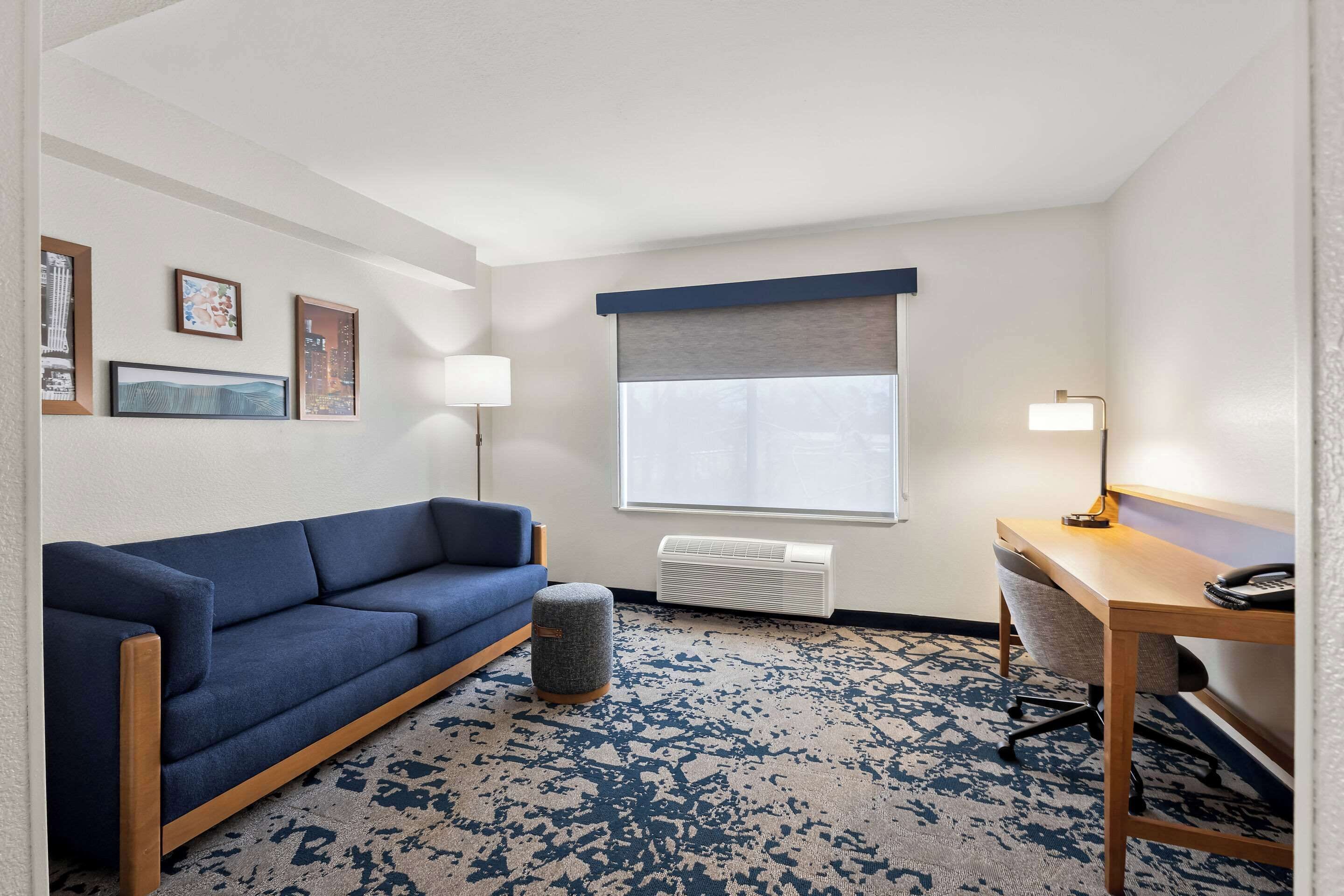 Ein Hotelzimmer mit einem blauen Sofa, einem Holztisch, einer Lampe und einem gemusterten Teppich.