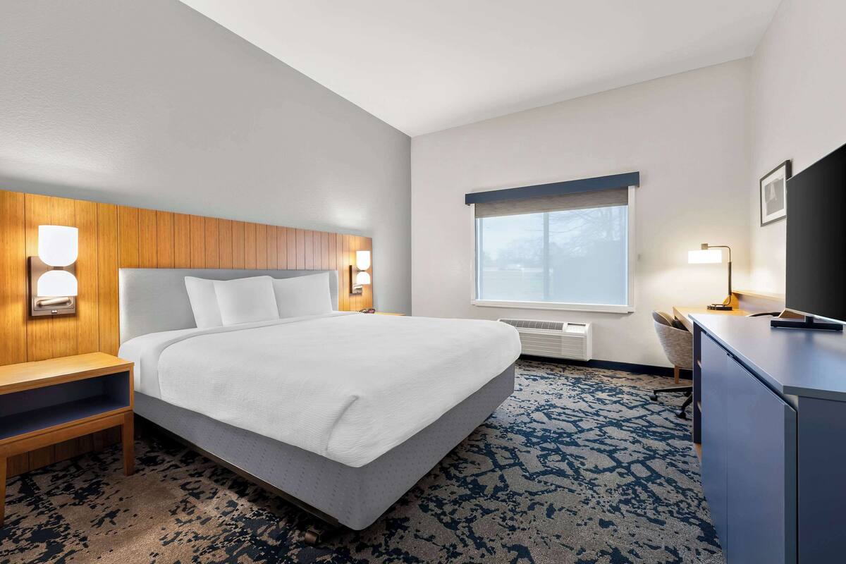 Habitación de hotel con una cama grande, un cabecero de madera, lámparas de noche, un escritorio con silla, un televisor y una ventana con vistas.
