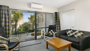 Un salon comprenant un canapé, deux fauteuils, une table basse en bois et une porte vitrée donnant sur une terrasse extérieure.
