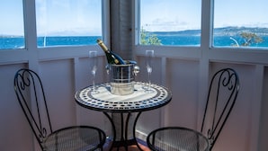 A balcony with two chairs, a table with a bottle of champagne and two glasses, and a view of the sea.