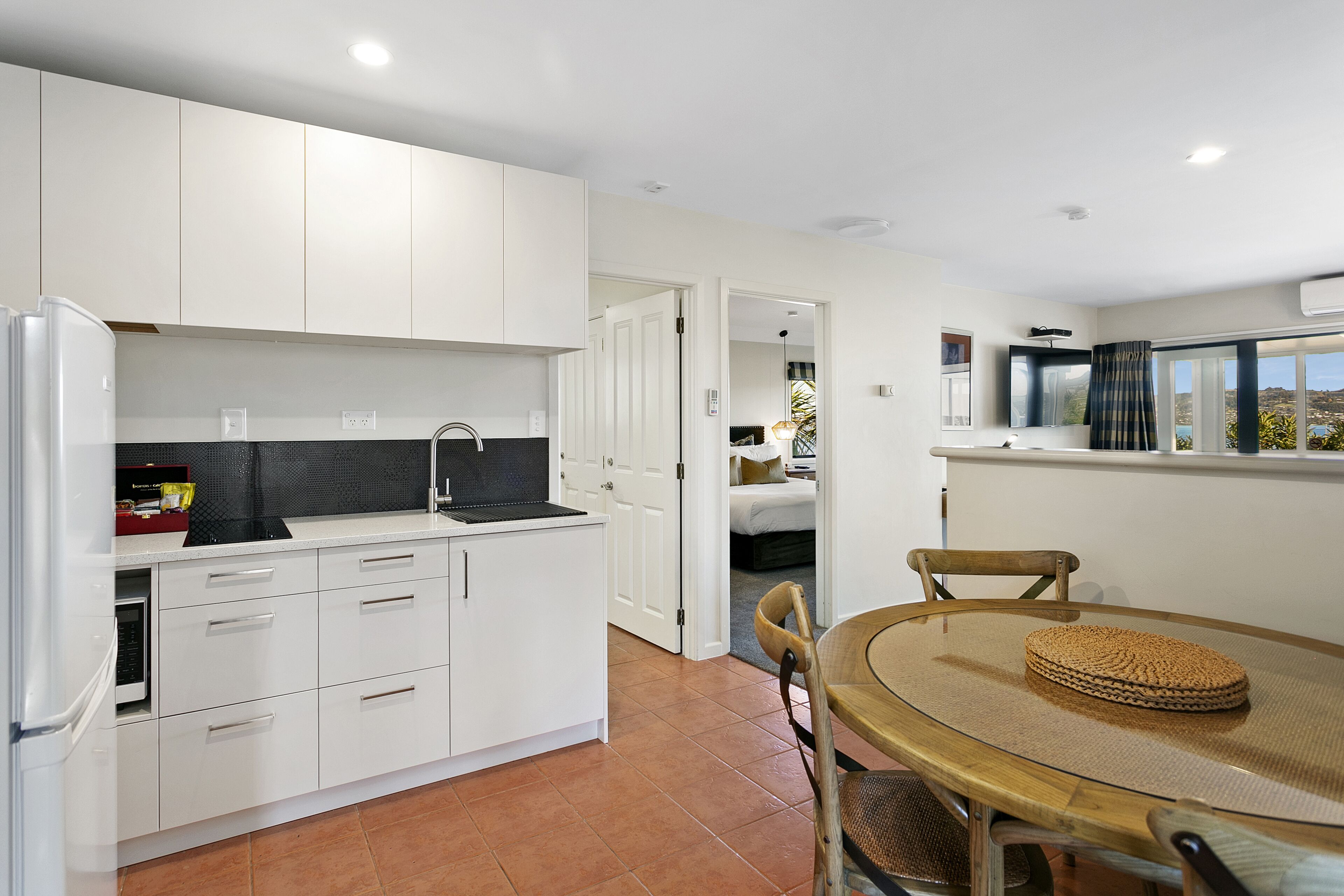 A modern kitchen with white cabinets, a built-in stove, and a dining area with a round table and chairs.