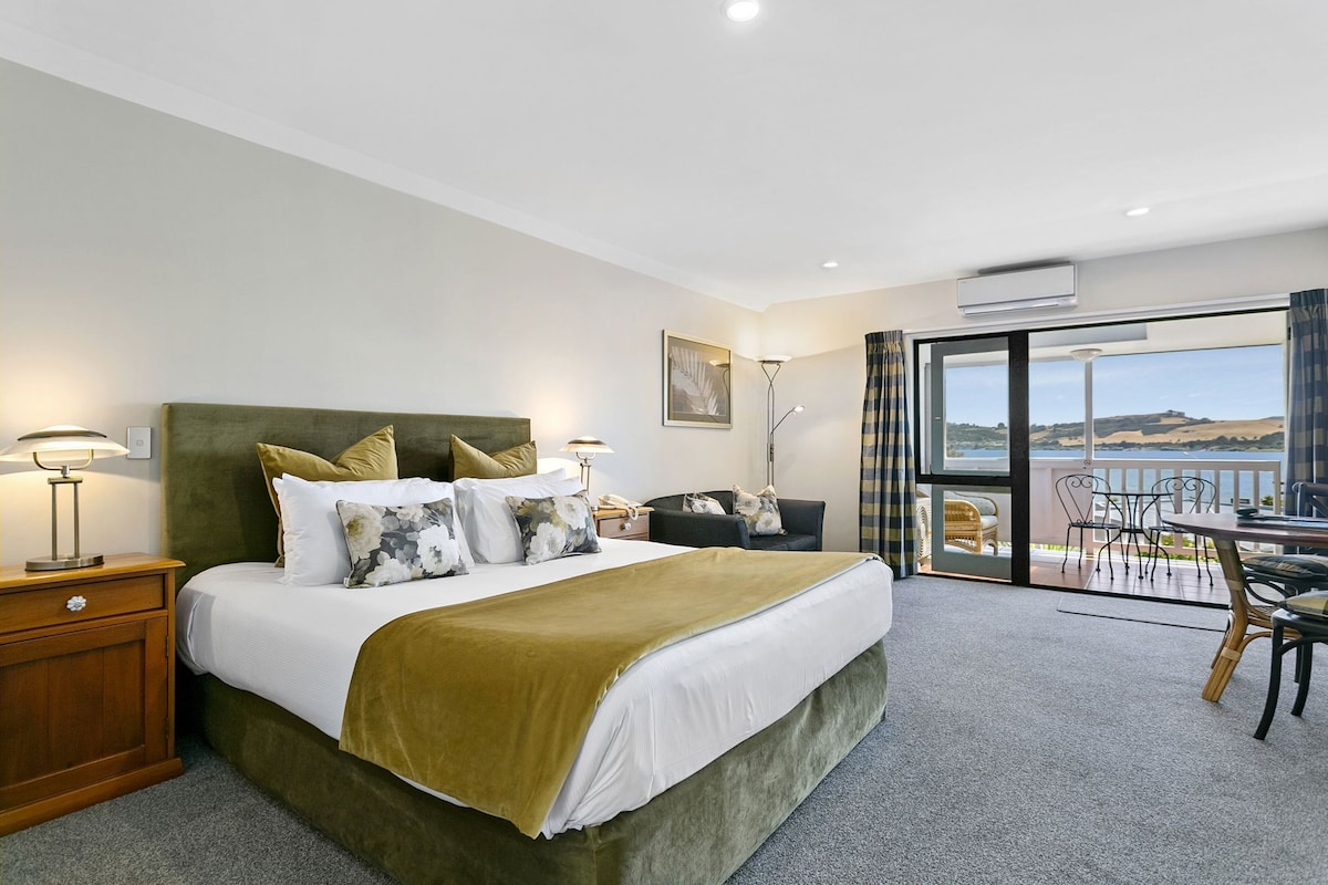 Habitación de hotel con una cama grande, un escritorio, una silla y un balcón con vistas.