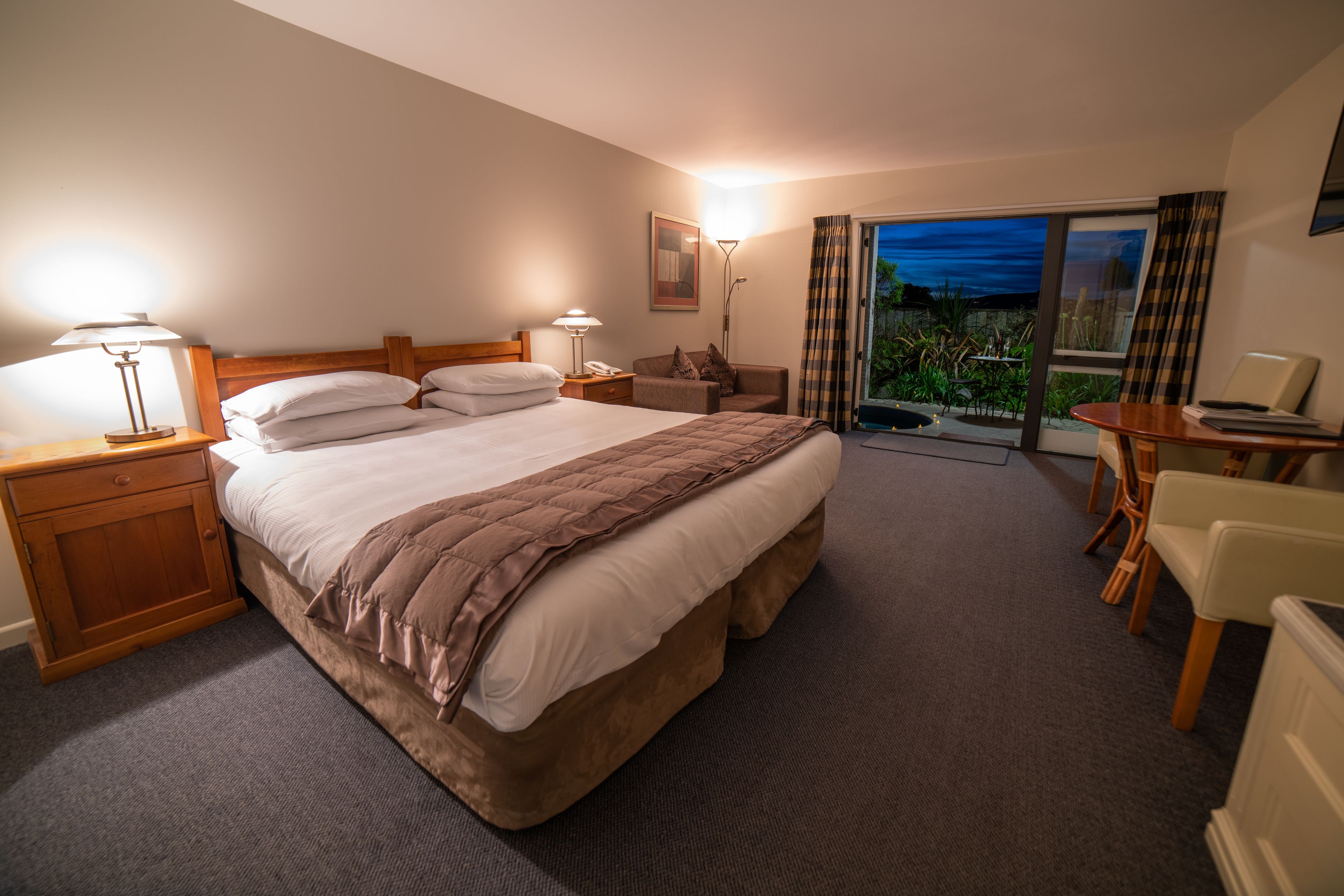 Ein Hotelzimmer mit einem großen Bett, Nachttischen, einem Schreibtisch und Blick ins Freie.