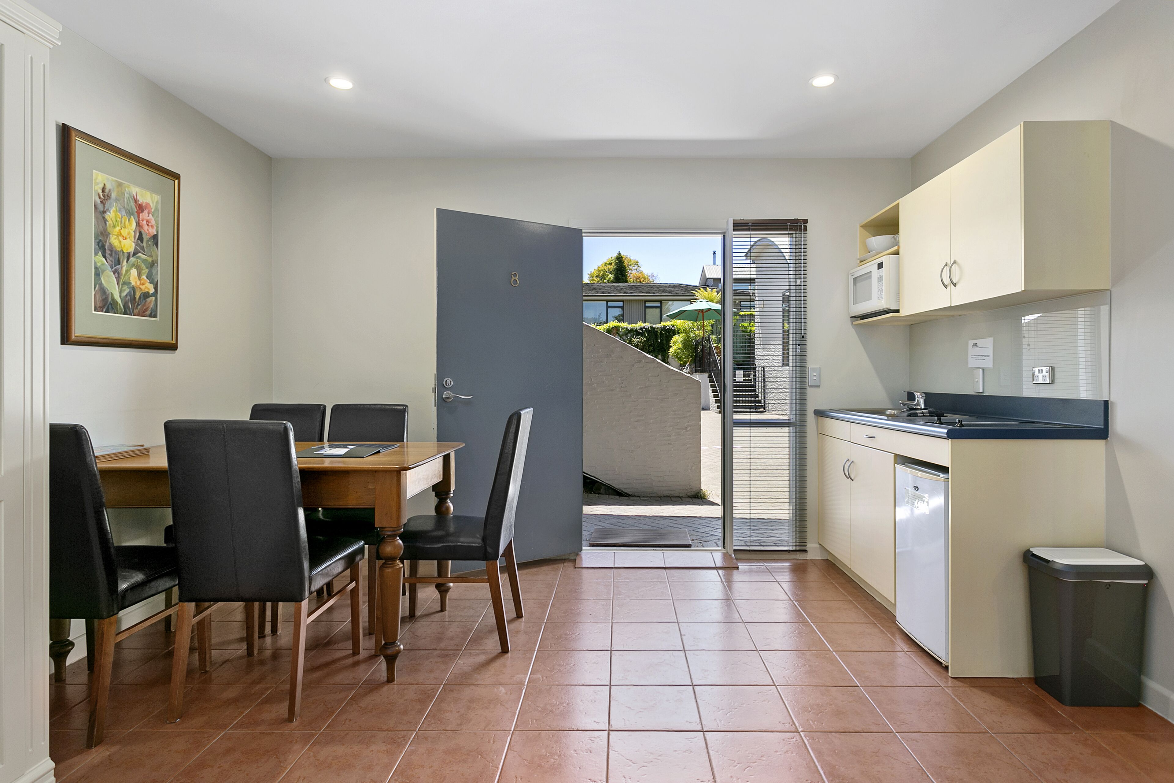 A compact kitchen with a dining area, a small trash bin, and a door leading to a balcony.