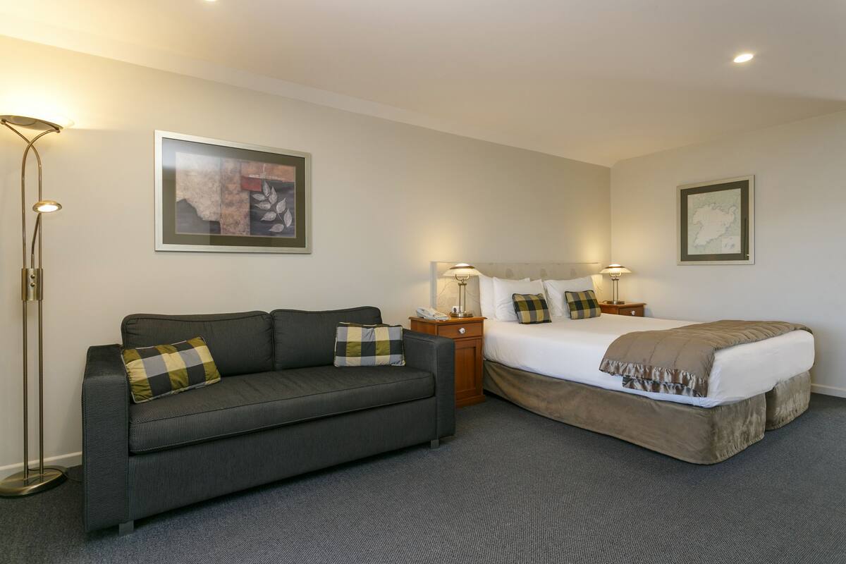 A hotel room with a bed, a sofa, a nightstand, and a floor lamp.