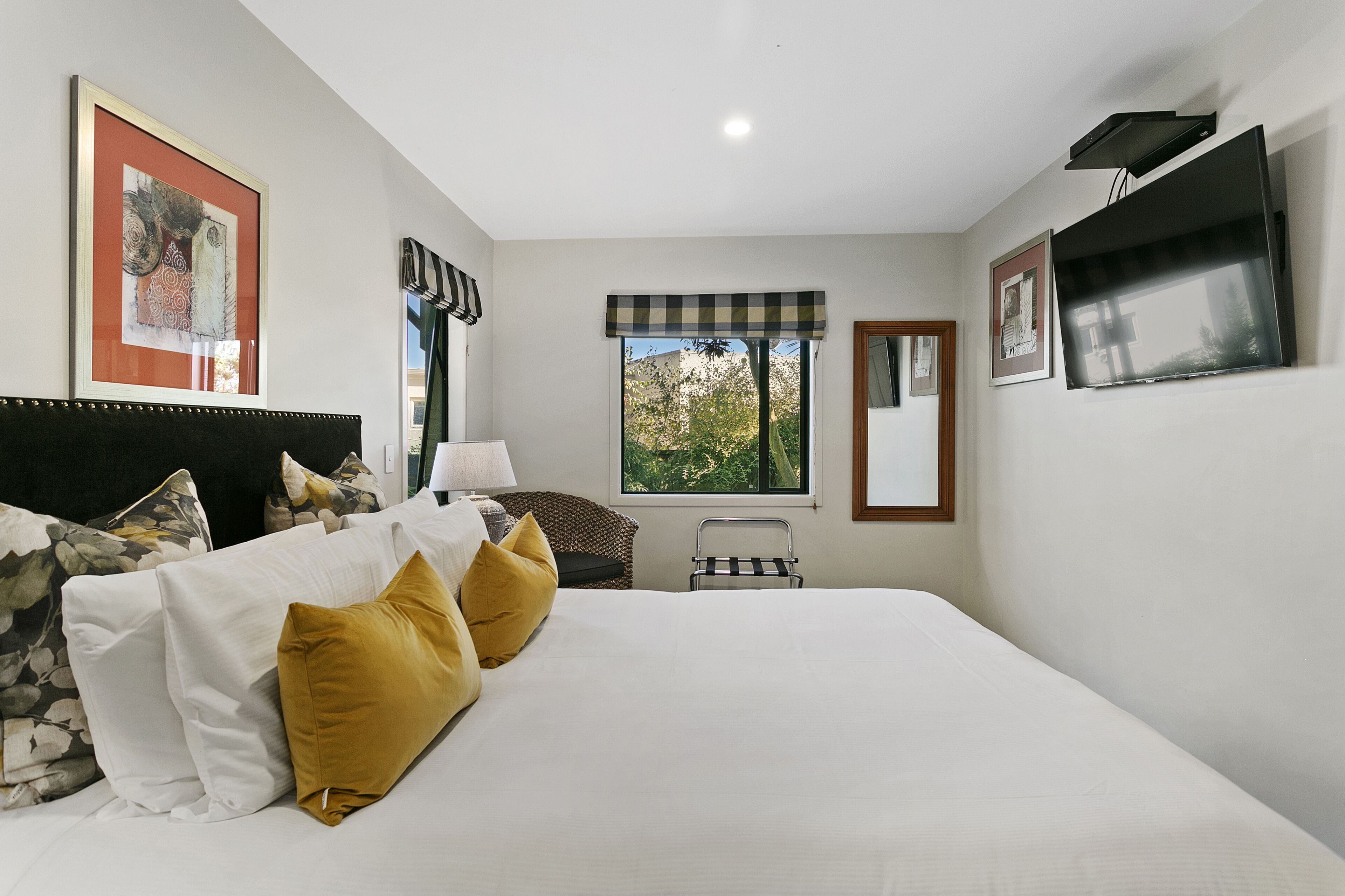 A hotel room with a large bed, a window with a view, a flat-screen TV, and artwork on the walls.