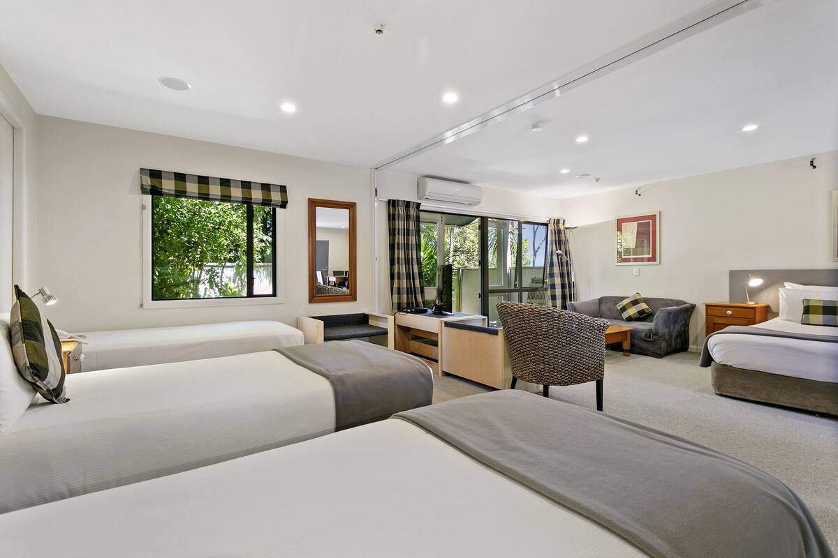 A modern hotel room with two beds, a desk, a chair, and a large window with curtains.