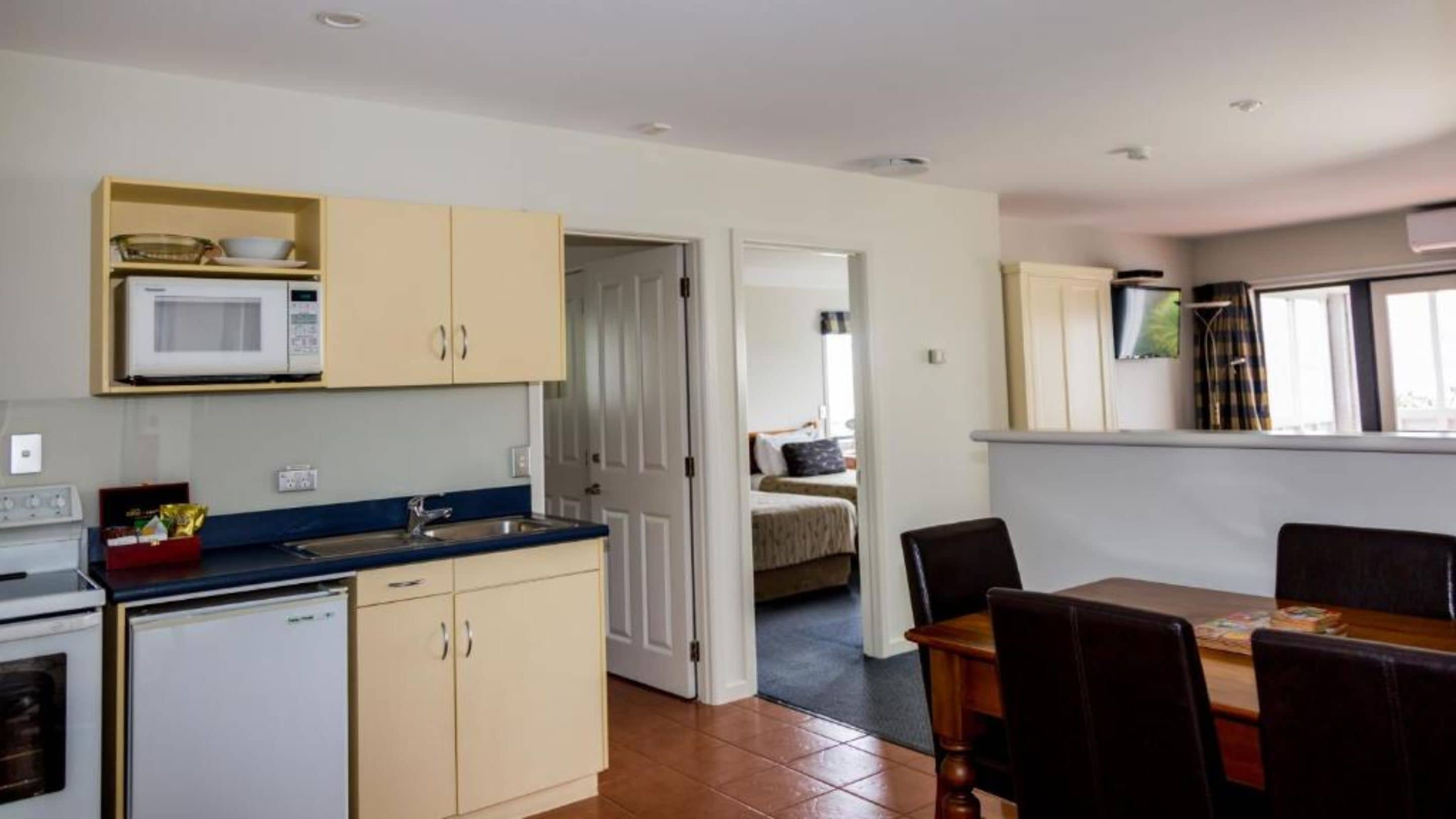 A compact kitchen with a microwave, sink, and cabinets. There's a dining area with a table and chairs, and a bed in the adjacent room.