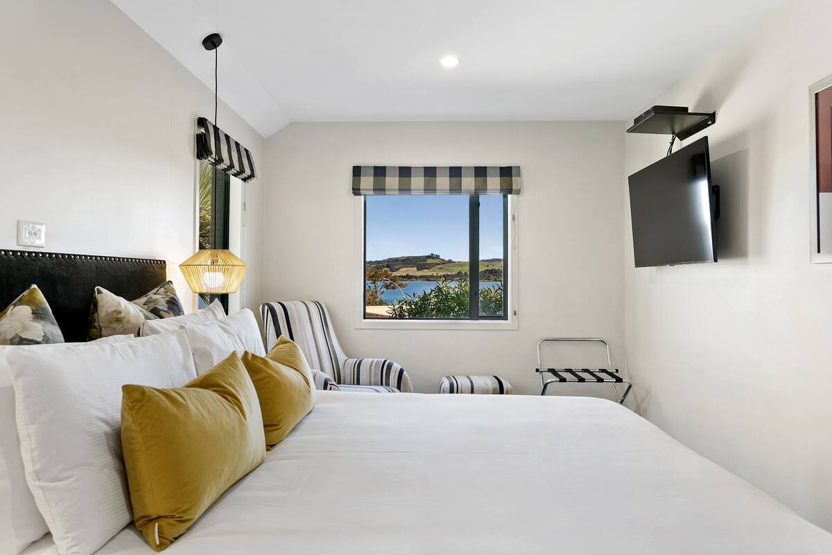 A bedroom with a bed, a TV, a window with a view of hills, and a lamp.