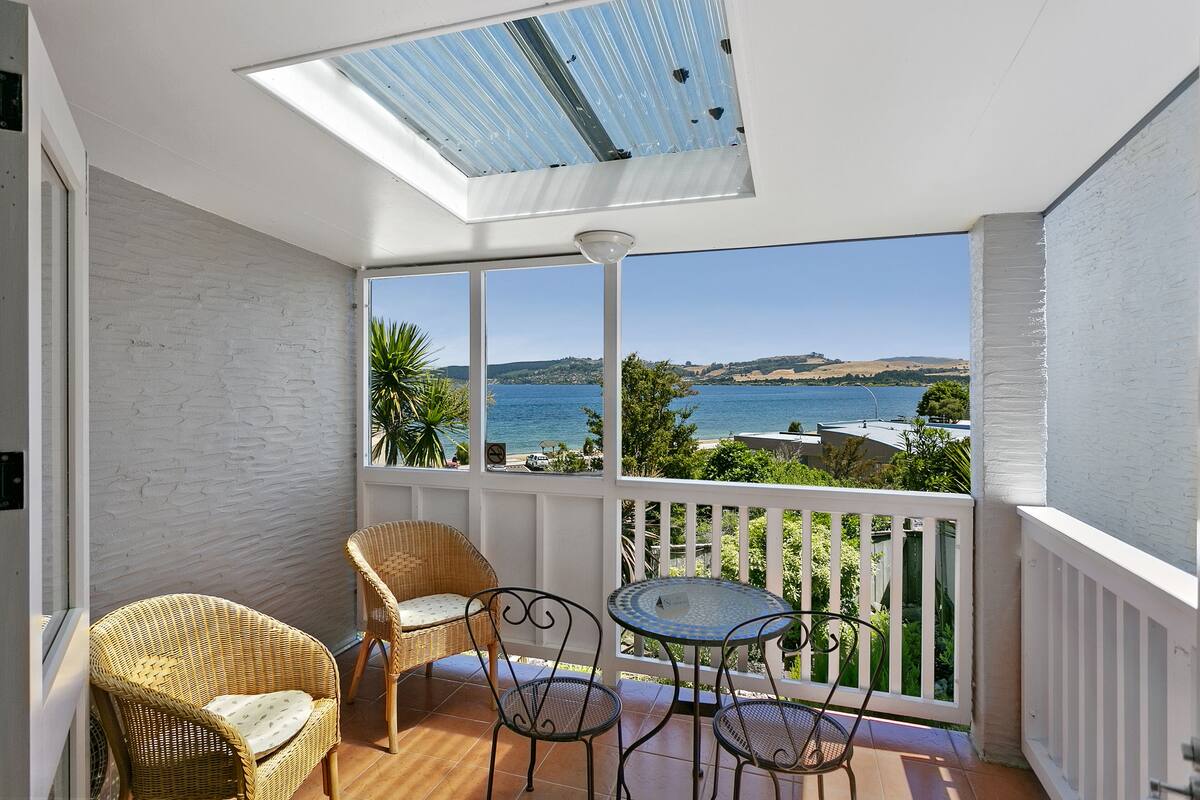 A balcony with a view of the sea, wicker chairs, a small table, and a white railing.
