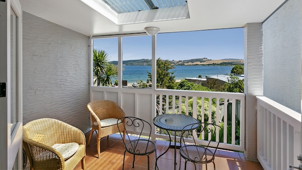 A balcony with a view of the sea, wicker chairs, a small table, and a white railing.