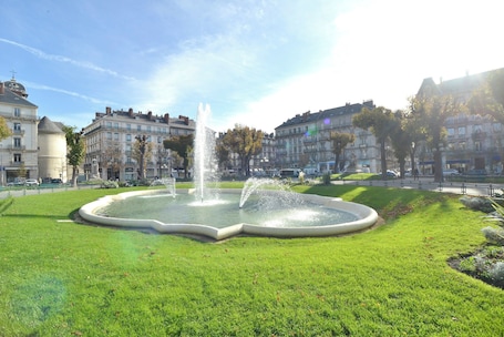 A fountain in a circular pool surrounded by a well-maintained lawn, with buildings in the background.. Hôtel d'Angleterre Grenoble Hyper-Centre