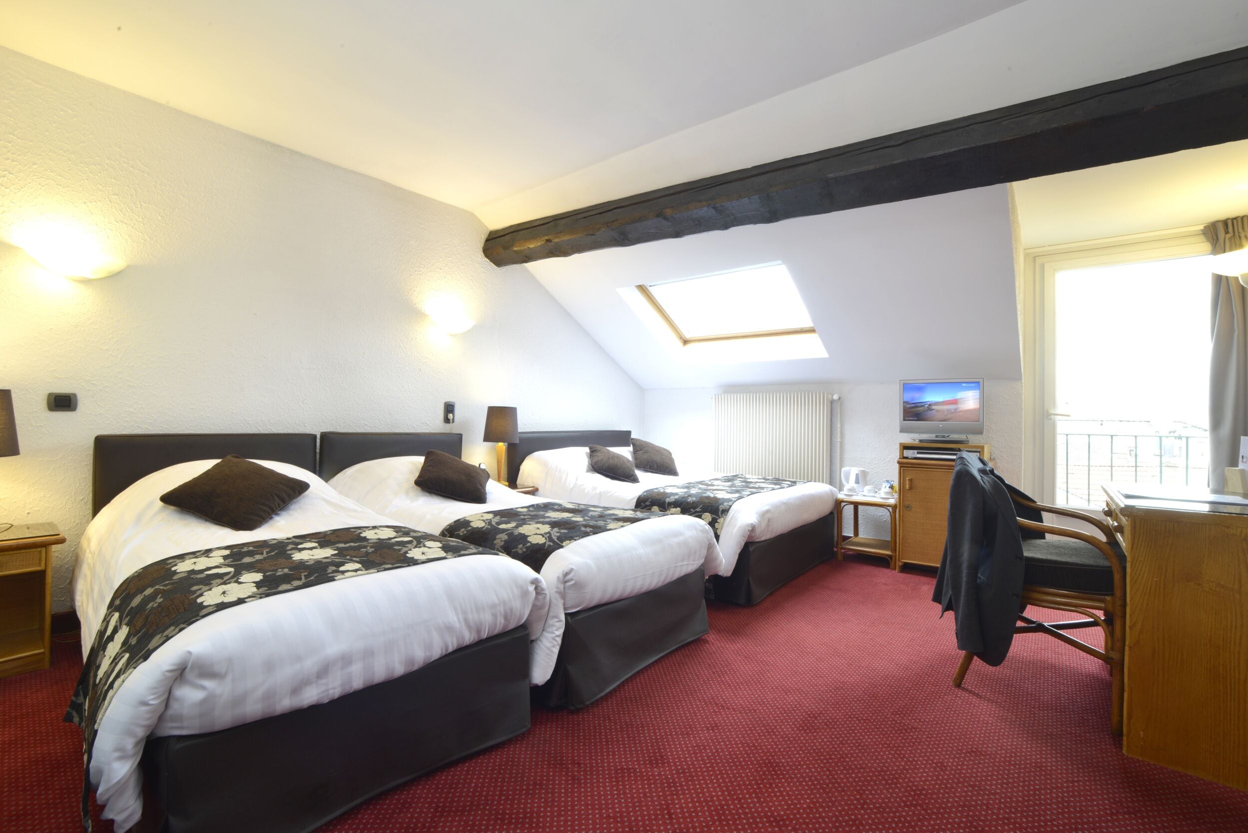 A hotel room with two beds, a desk, a television, and a window with curtains.