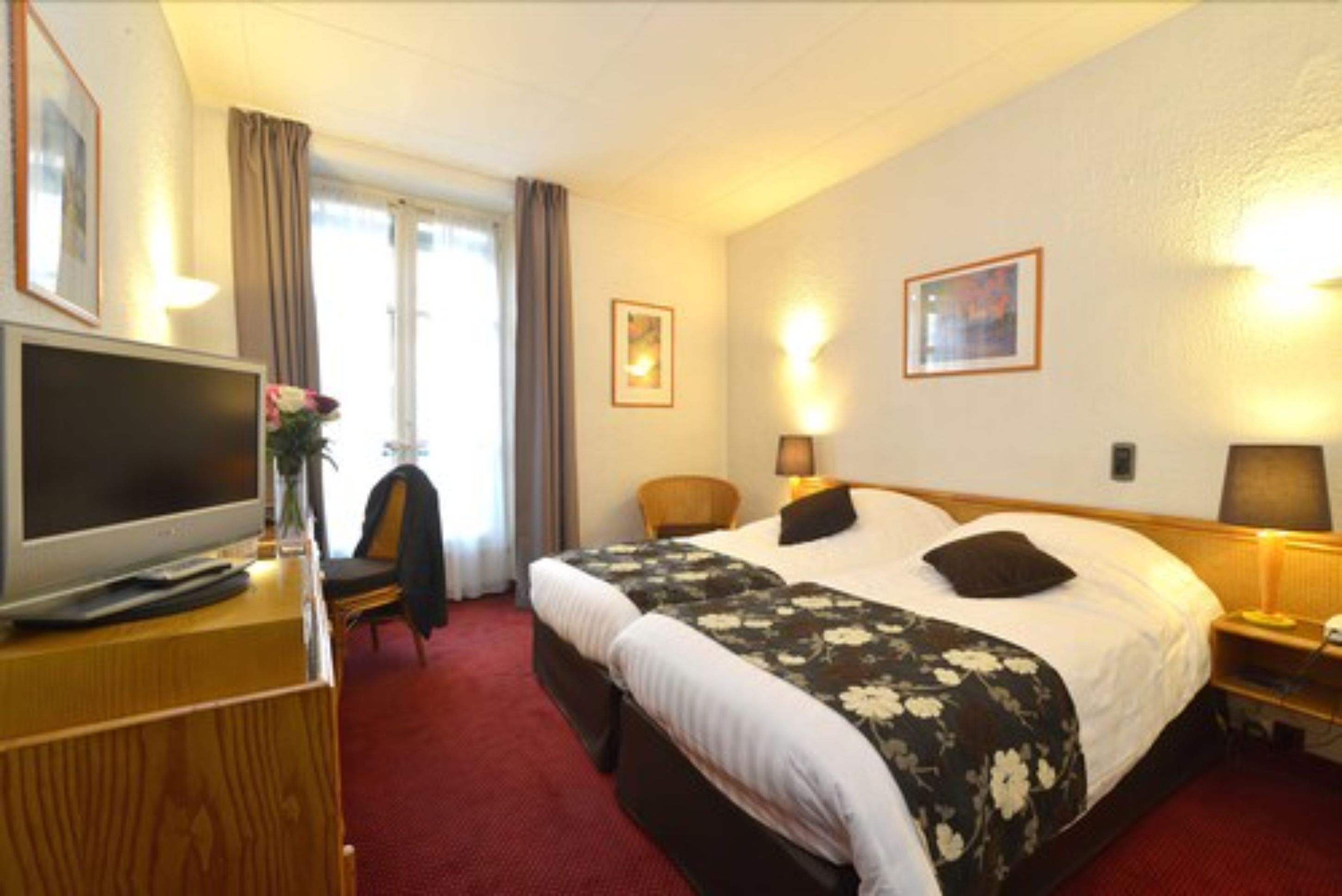 Ett hotellrum med en stor säng, ett skrivbord med en platt-TV, en stol och ett fönster med gardiner.