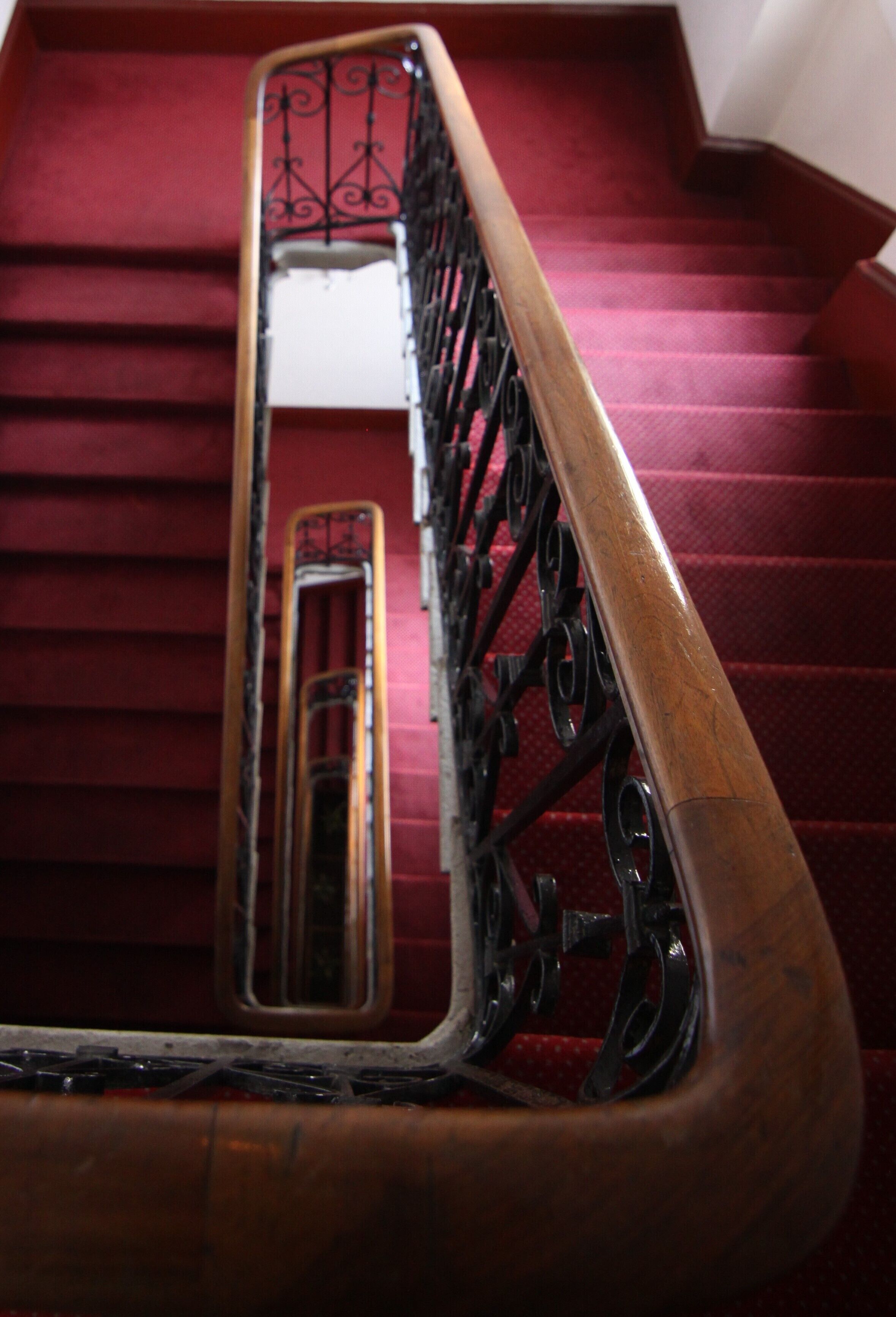 Una escalera con barandilla de madera y barandillas de metal negro, que conduce a una habitación con piso cubierto de alfombra roja.