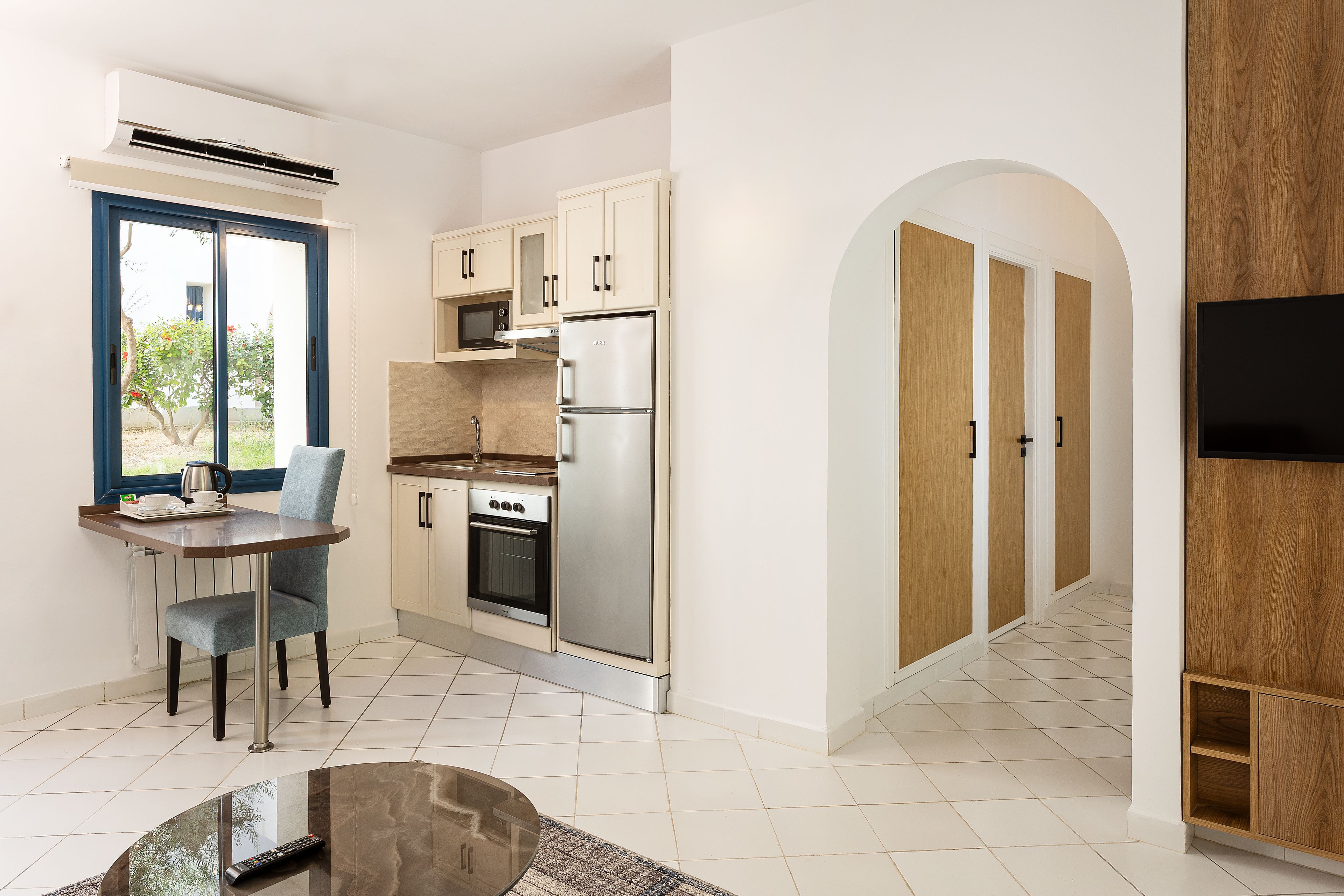 Una cucina moderna con forno a incasso, microonde e frigorifero. C'è un'area pranzo con tavolo e sedie, e una finestra con vista sul verde.