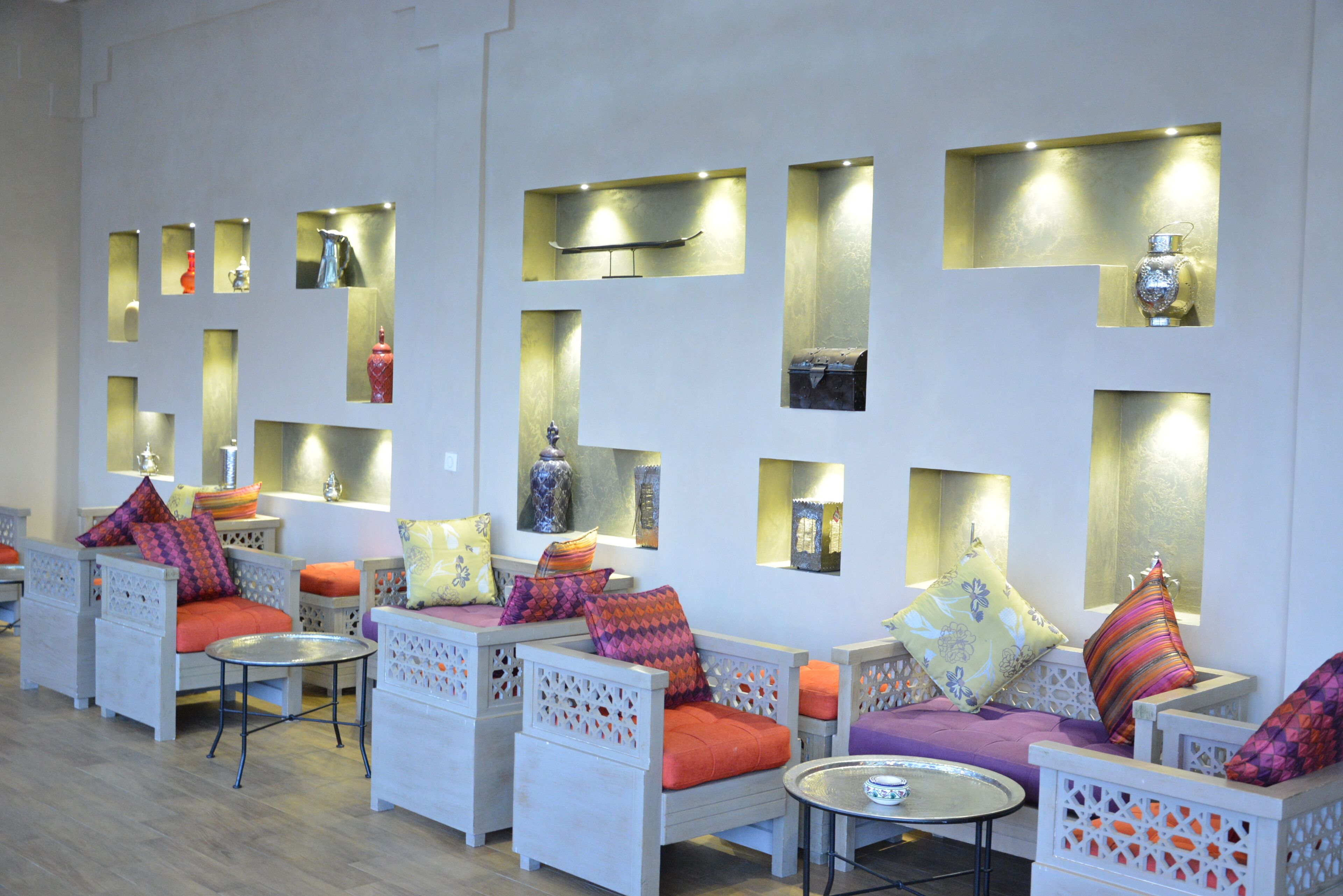 A modern lounge area with white wicker furniture, orange cushions, and decorative wall panels.
