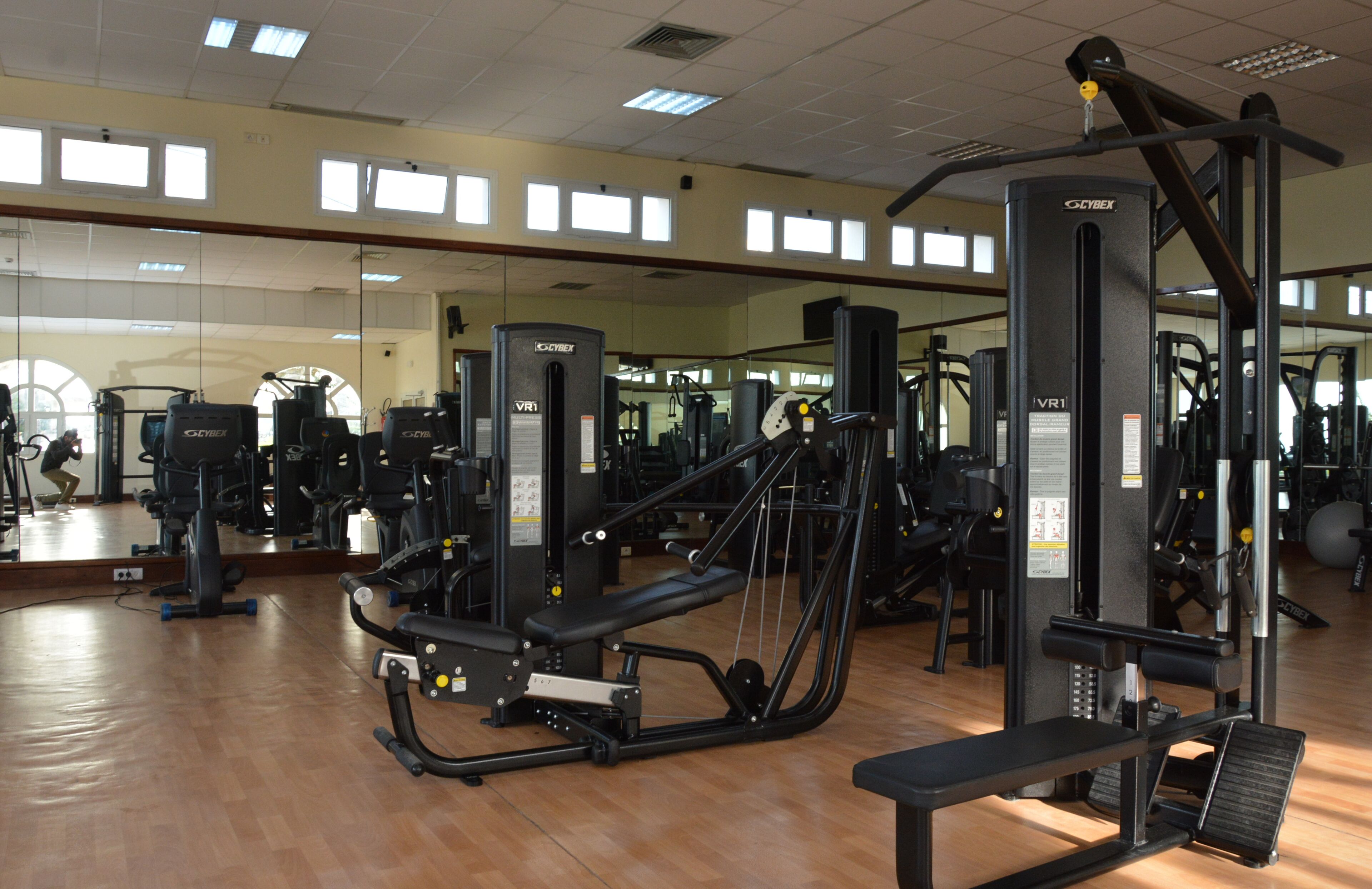 A gym with various exercise machines, mirrors, and a wooden floor.