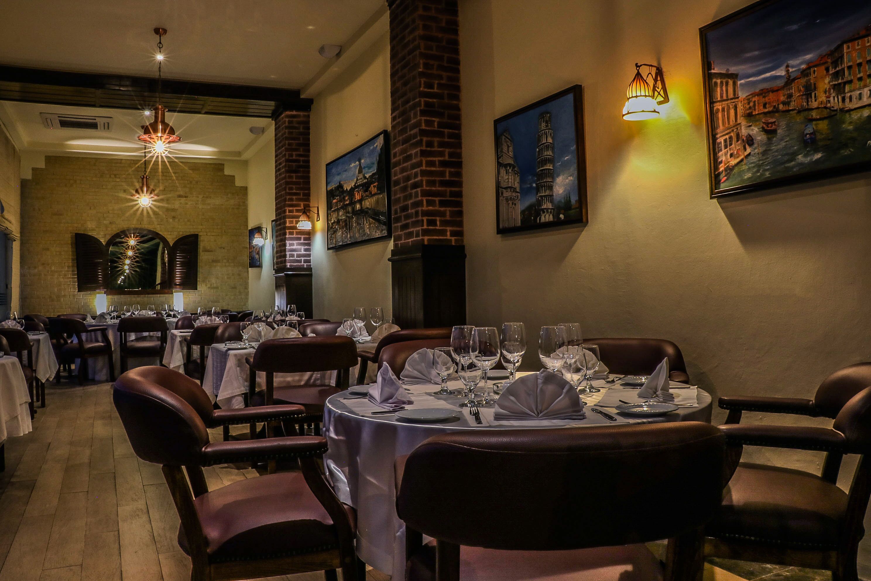 A restaurant with round tables set with white tablecloths and brown leather chairs.
