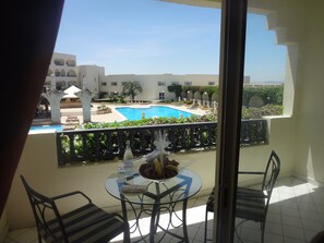 A balcony with a glass table, two chairs, and a view of a swimming pool and buildings in the background. - Golden Carthage Hotel & Résidence (La Marsa)