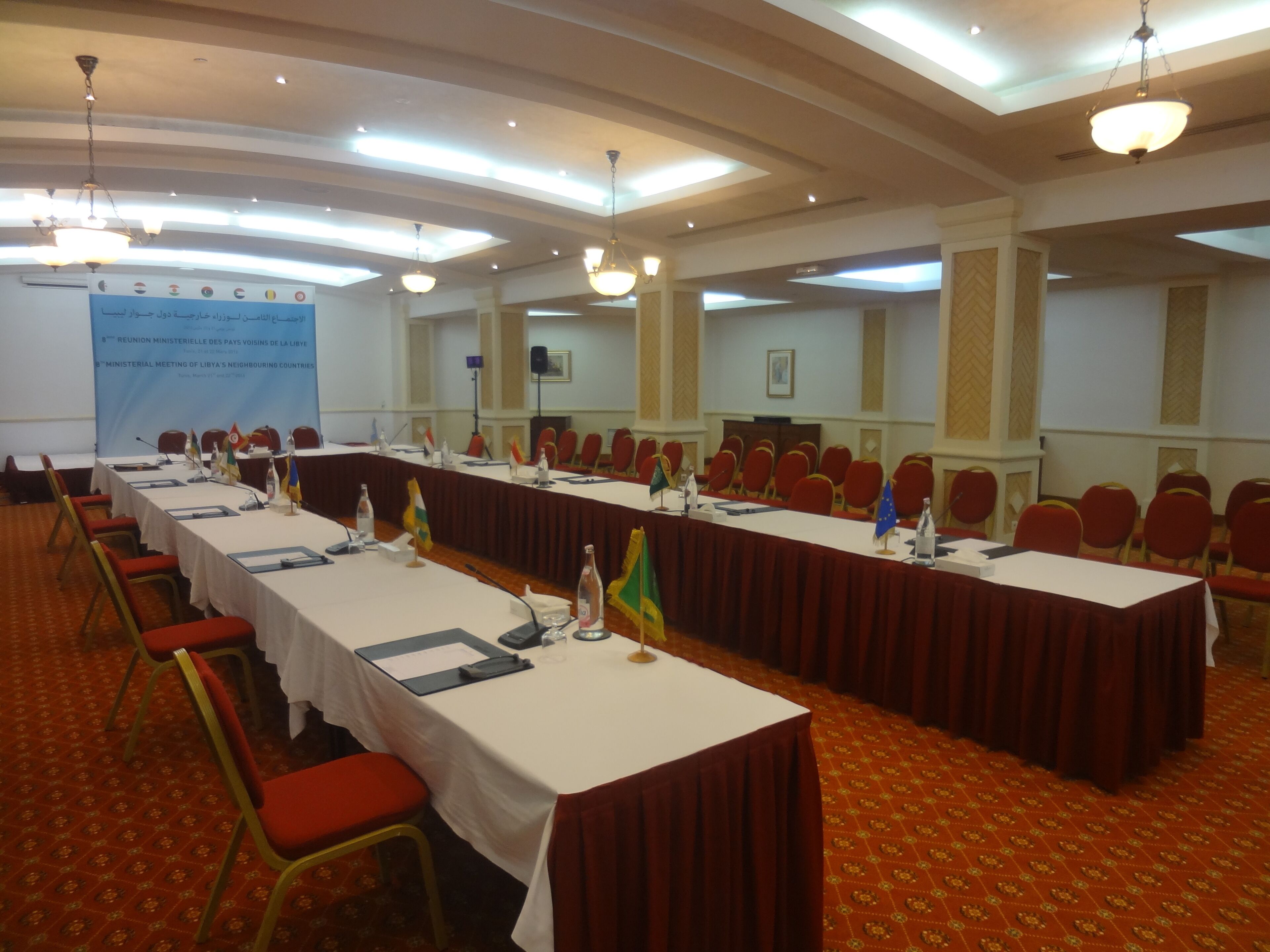 A conference room with long tables, red chairs, and a projector screen displaying text.
