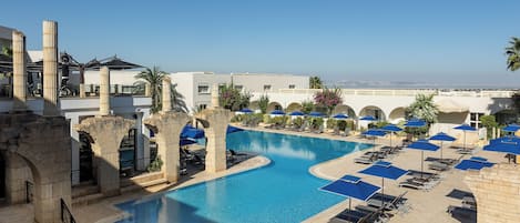A pool area with lounge chairs and umbrellas, a clear sky, and a view of the sea.