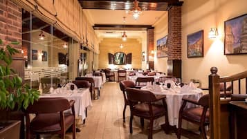 A restaurant with multiple tables set for dining, featuring brick walls and wooden beams.