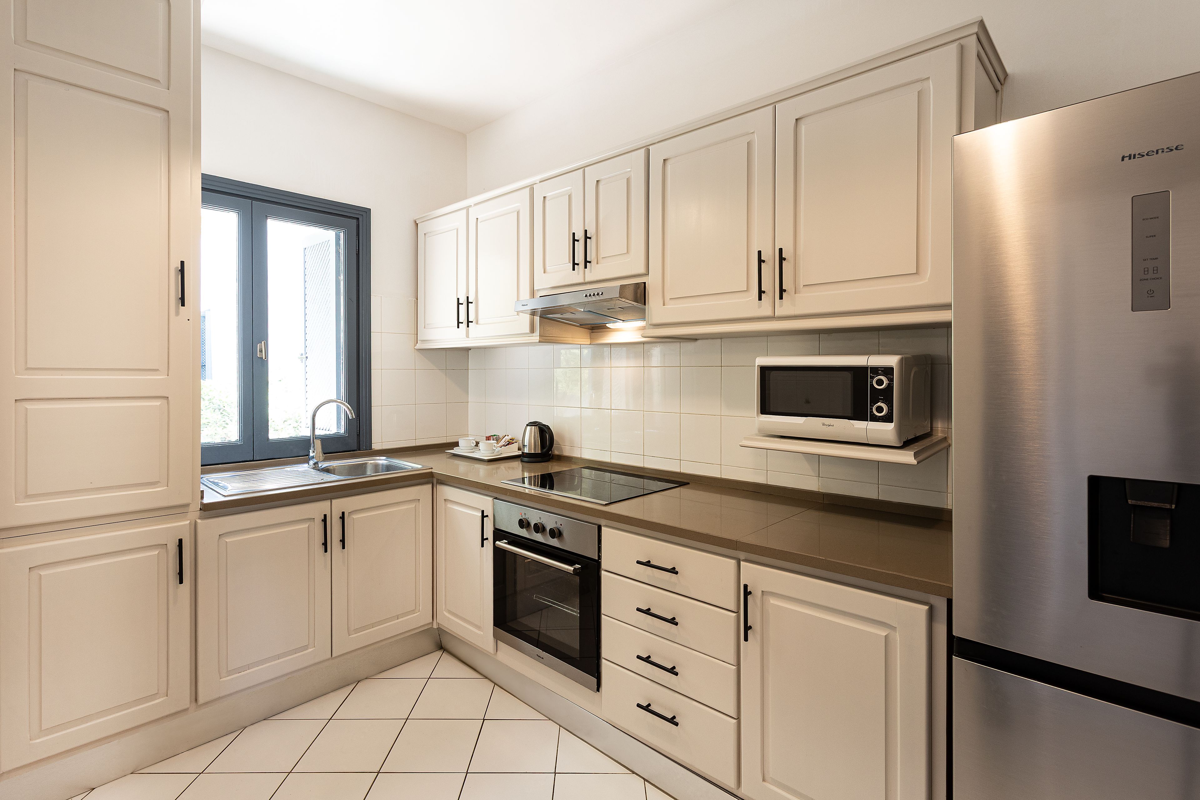 Una cocina moderna con armarios blancos, un refrigerador de acero inoxidable, un microondas, un horno y un ventanal con vistas.