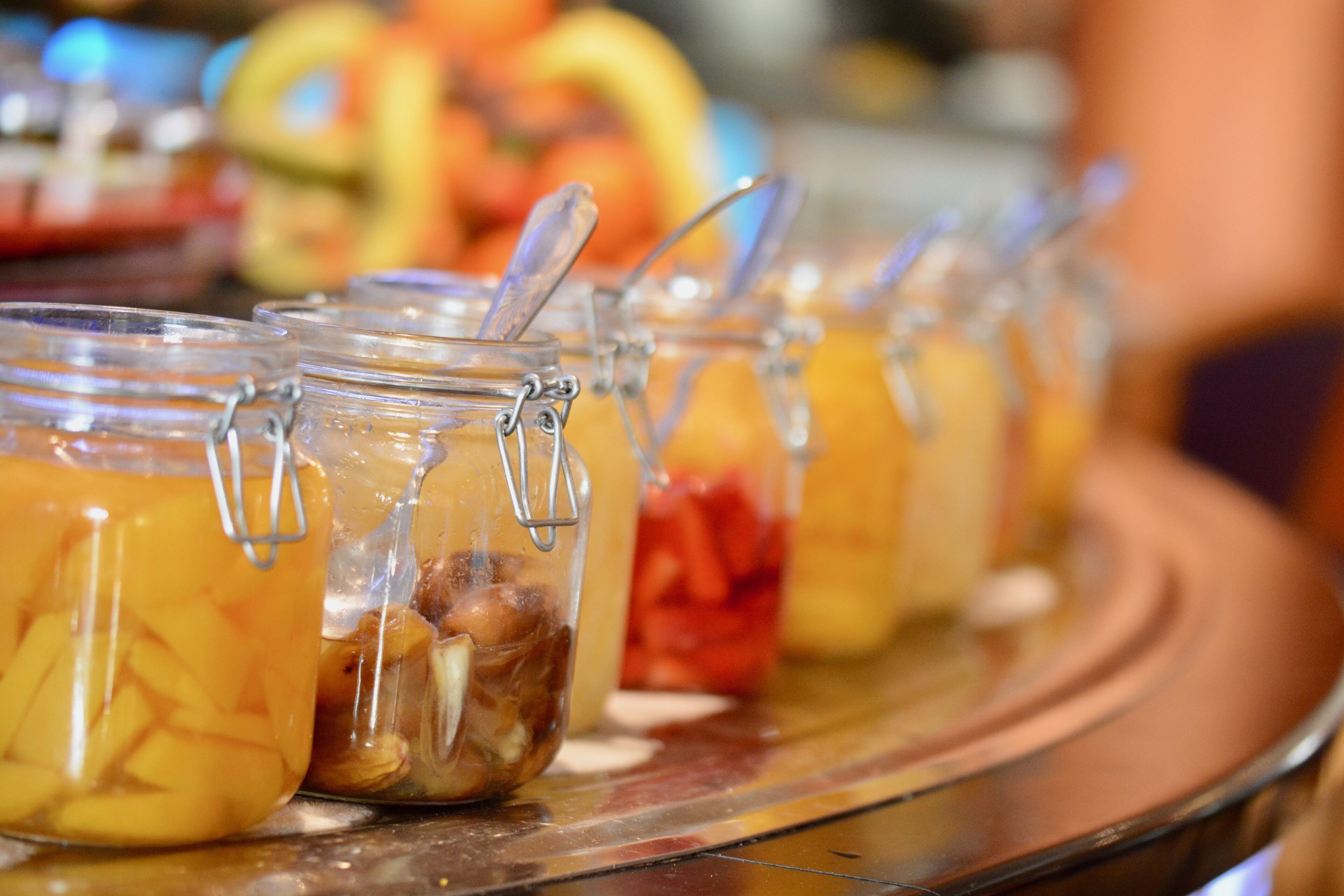 A row of glass jars with metal clasps, containing various food items, displayed on a metal tray.