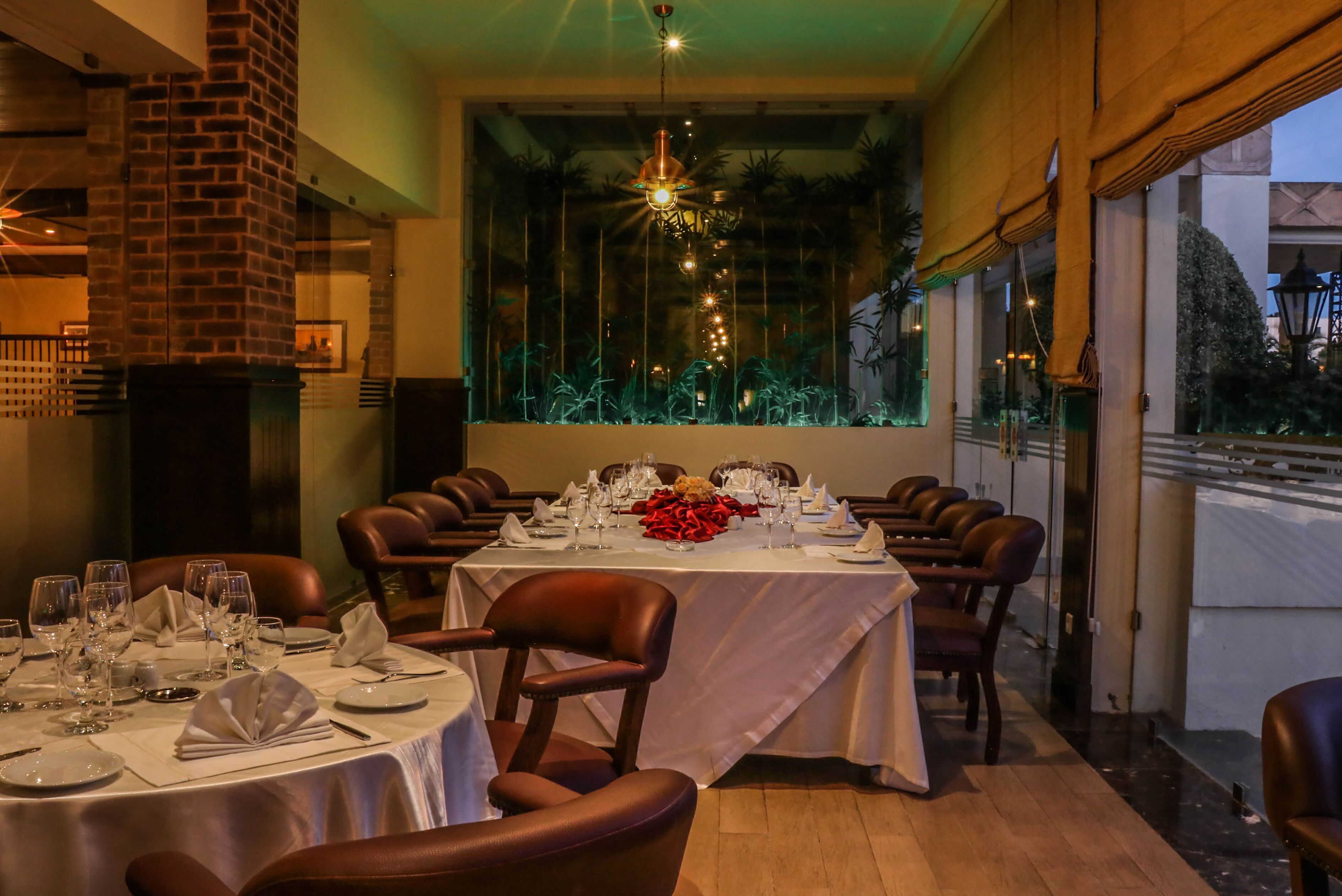 A restaurant with round tables set for dining, leather chairs, and a view through large windows.