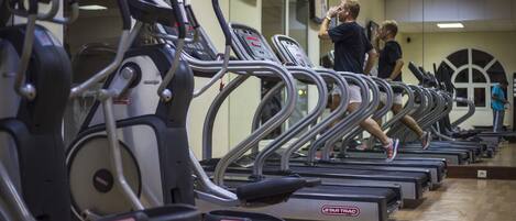 Un gimnasio con varias cintas de correr alineadas frente a un espejo grande.