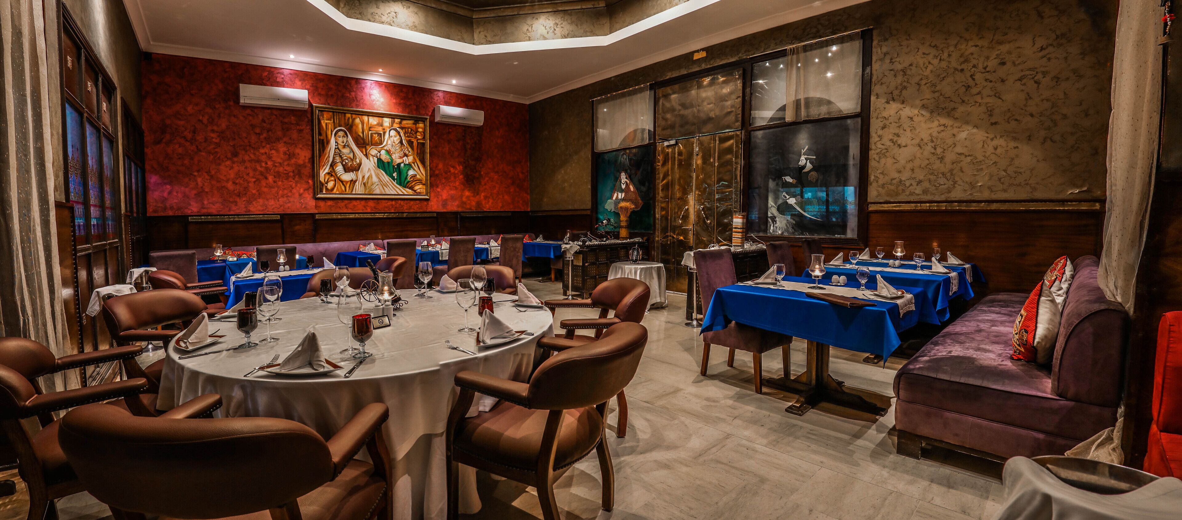 Ein Restaurant mit runden Tischen, braunen Ledersesseln und blauen Tischdecken.