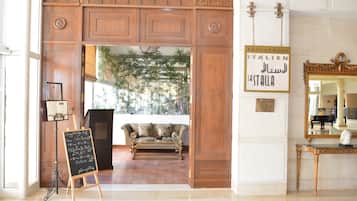 Un vestíbulo de hotel con un mostrador de recepción de madera, una pizarra con artículos del menú, un sofá y un letrero que indica que el restaurante es italiano.