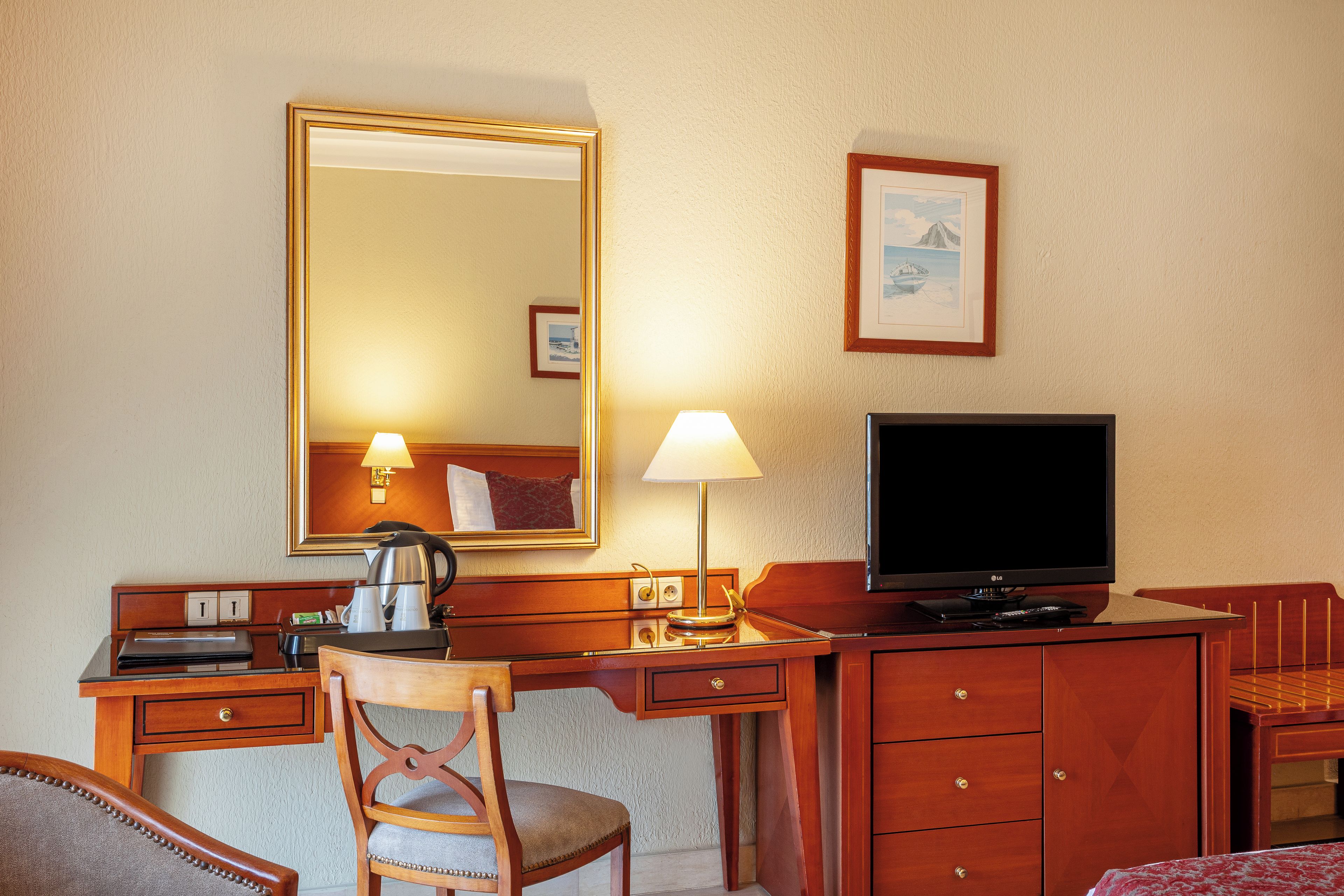 Une chambre d’hôtel avec un bureau en bois, une chaise, une télévision, un miroir et une lampe.