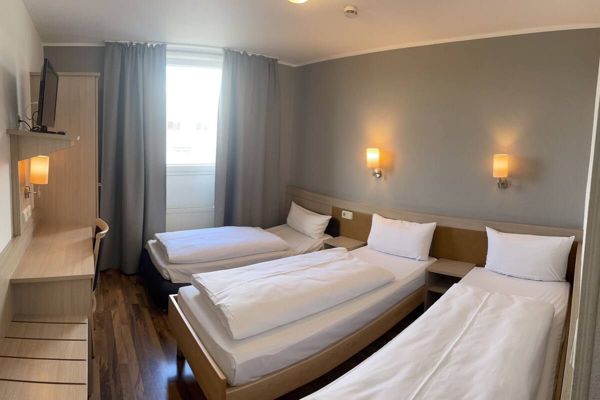 Et hotelværelse med to senge, et skrivebord, en stol, et fjernsyn og et vindue med gardiner.