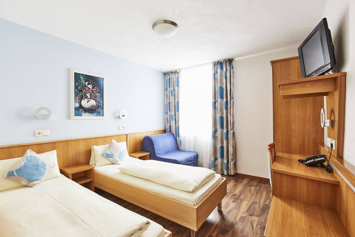 Et hotelværelse med to senge, et fjernsyn på et træstel, et billede på væggen og et vindue med gardiner.
