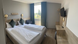 A hotel room with two beds, a TV, a desk, and a window with curtains. - Hotel Imperial (Munich)