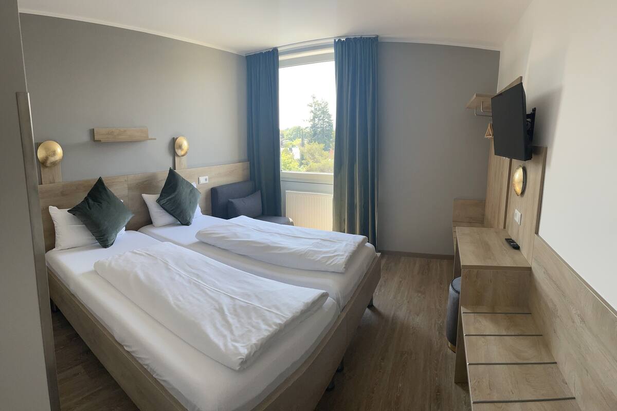 Et hotelværelse med to senge, et fjernsyn, et skrivebord og et vindue med gardiner.